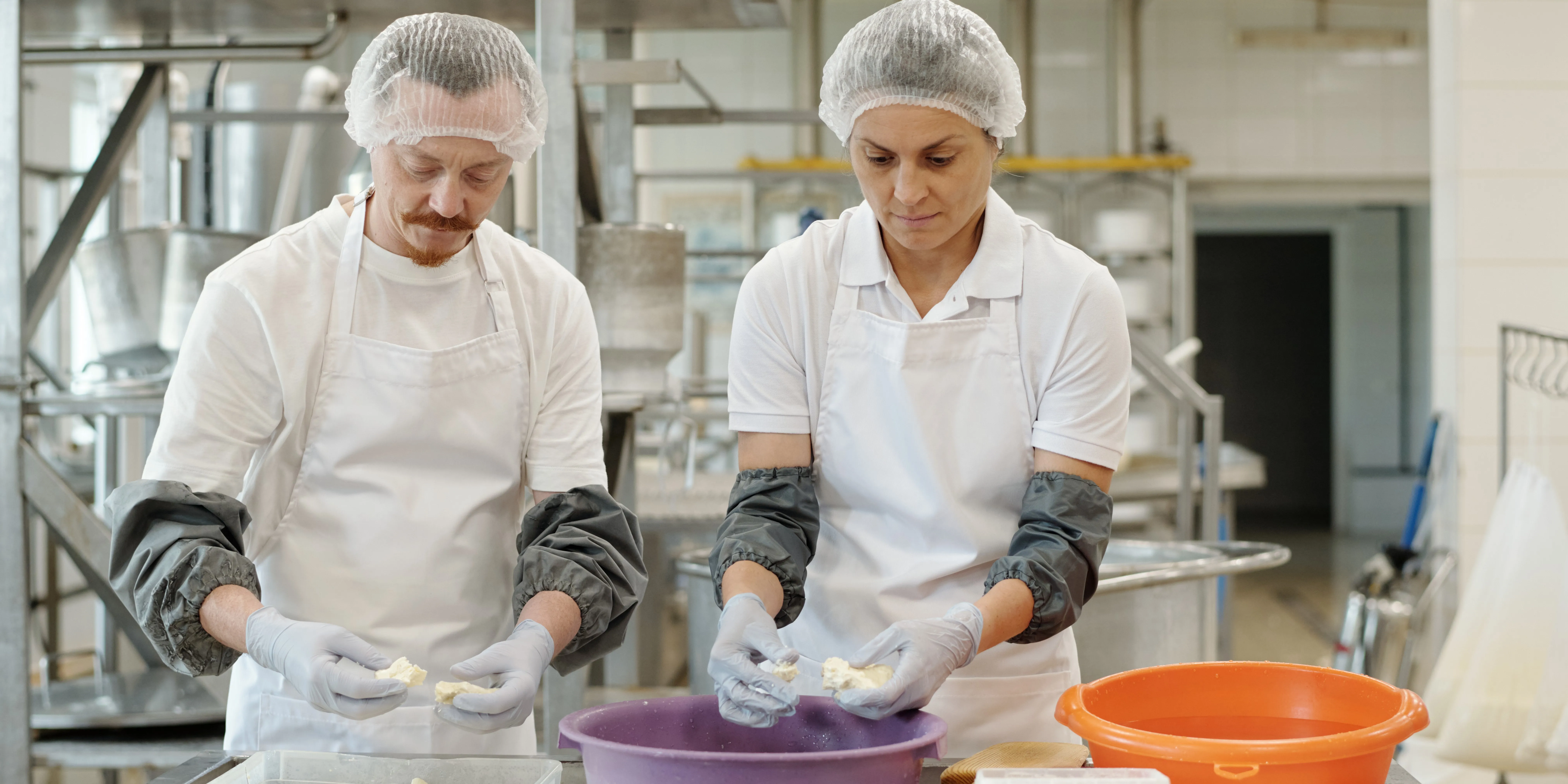 workers in protective clothing processing cheese in a food production facility