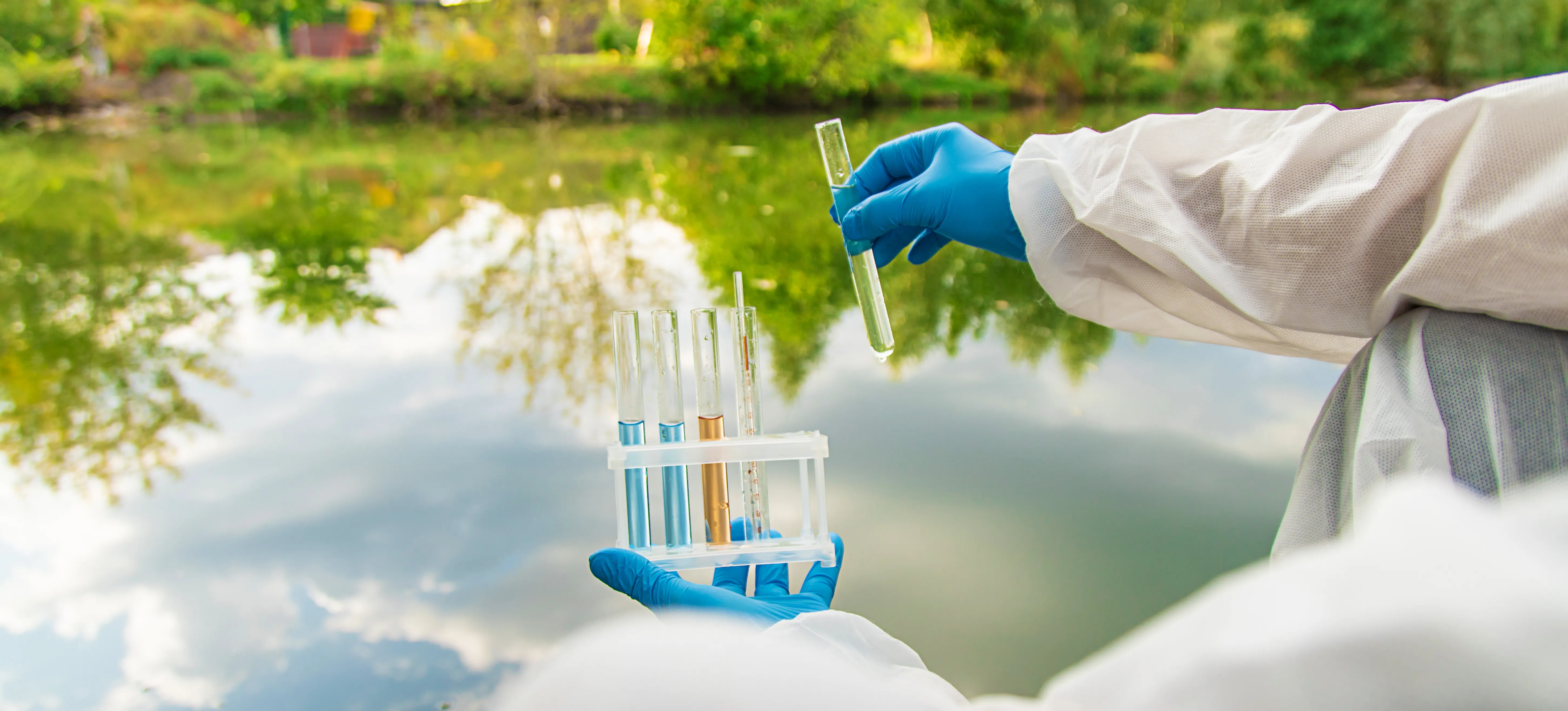 gloved hand holding test tube by river