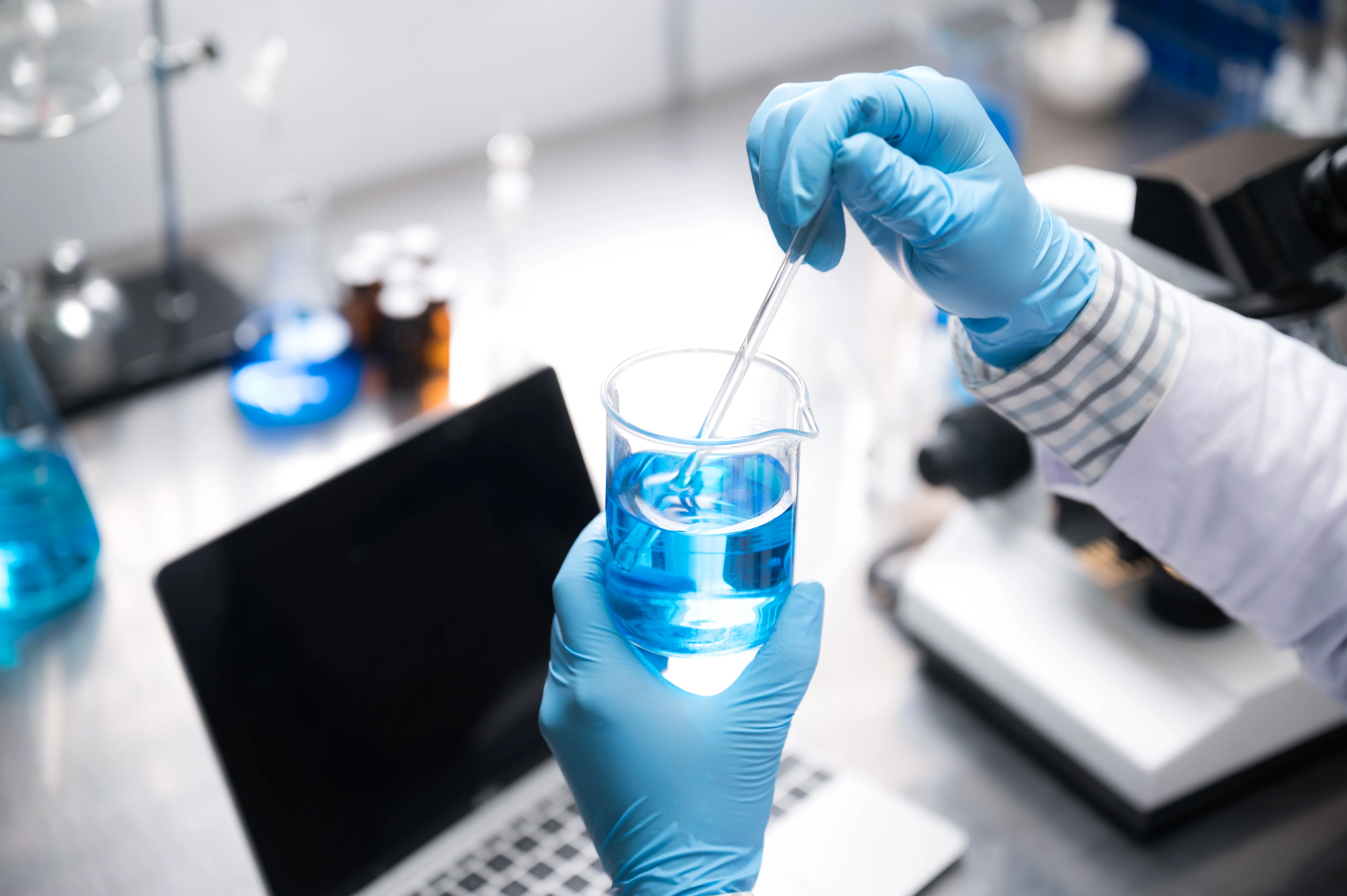 gloved hands mixing blue liquid in beaker