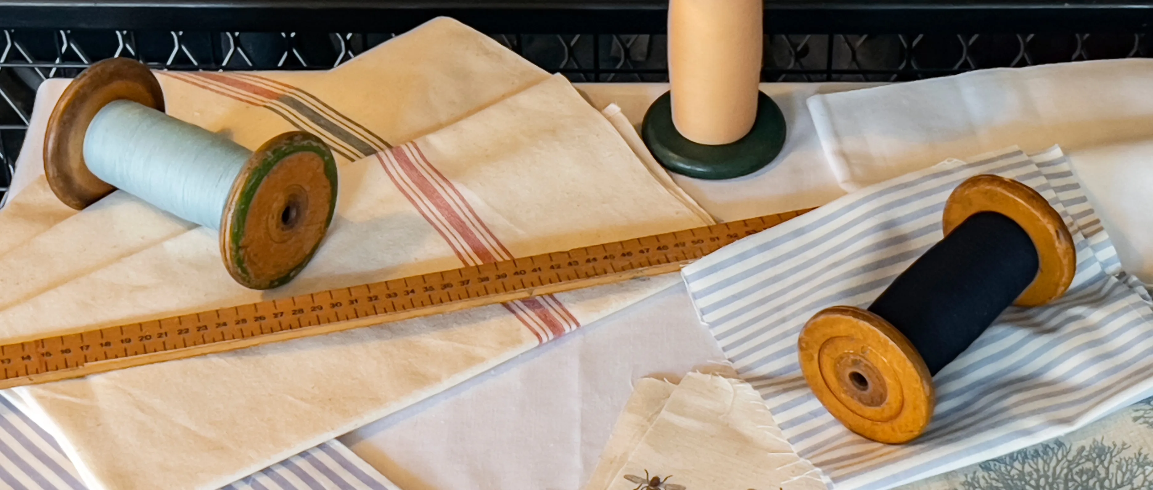 Vintage wooden spools with thread on striped and plain fabrics.